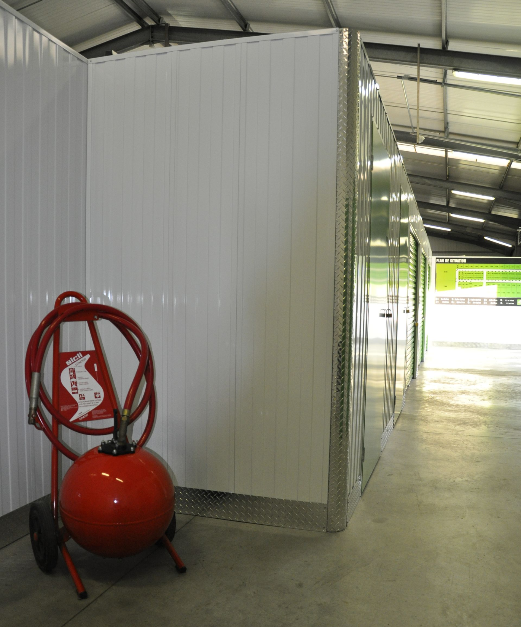 Des conteneurs de stockage en tôle ondulée blanche avec une porte verte ouverte. À l'intérieur, on aperçoit un autre conteneur.