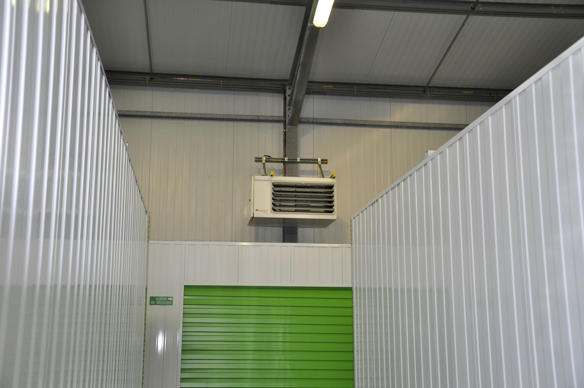 Vue intérieure d'un couloir d'entrepôt avec des murs blancs ondulés et une porte verte.