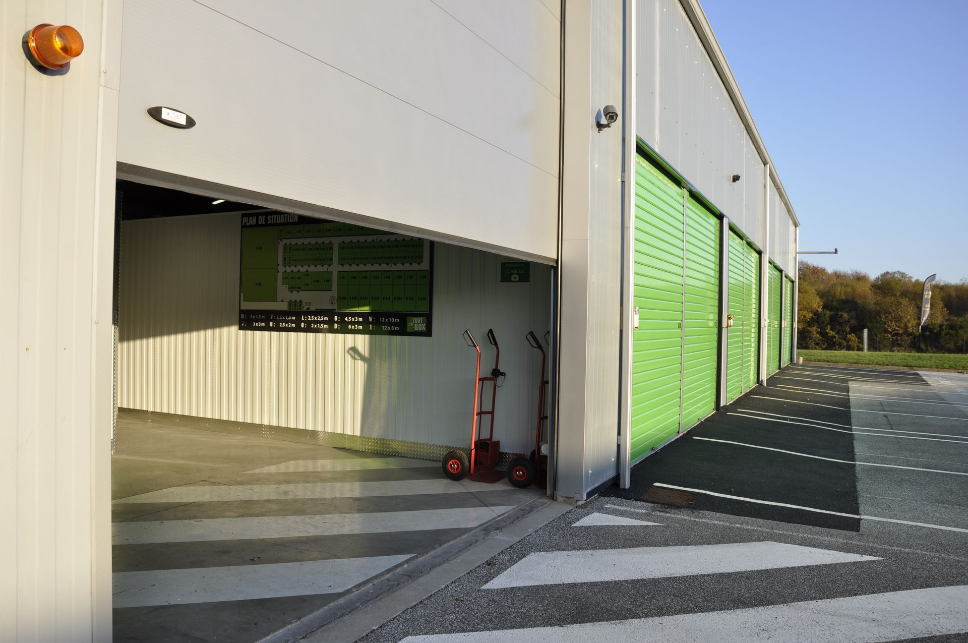 Des box de stockage aux portes vertes et un bâtiment blanc. Une porte est ouverte, laissant entrevoir l'intérieur.