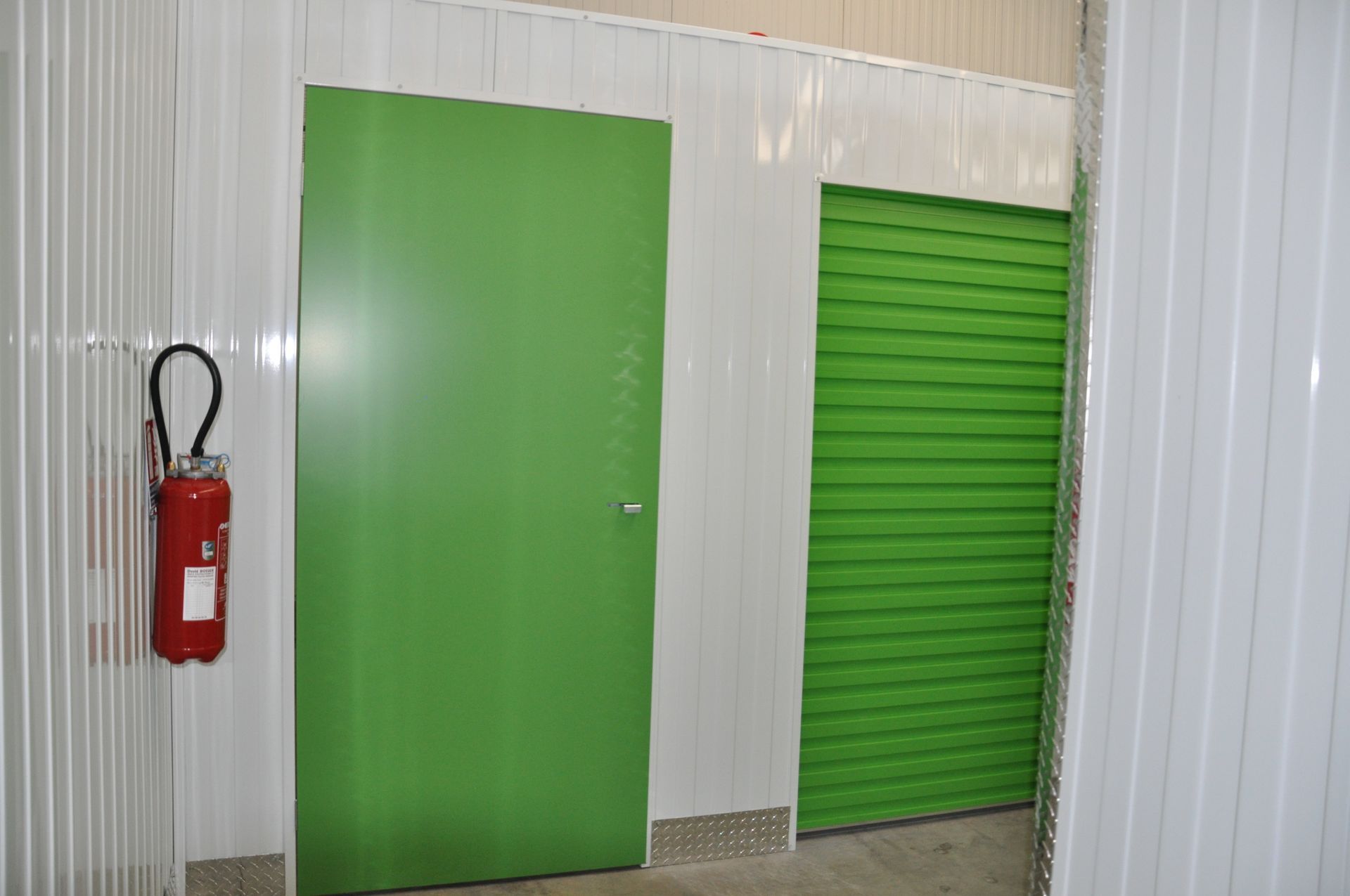 Des portes vertes dans un box de stockage, avec un extincteur rouge au mur.