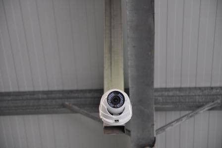 Caméra de sécurité fixée sur une poutre de support métallique, devant un plafond blanc.