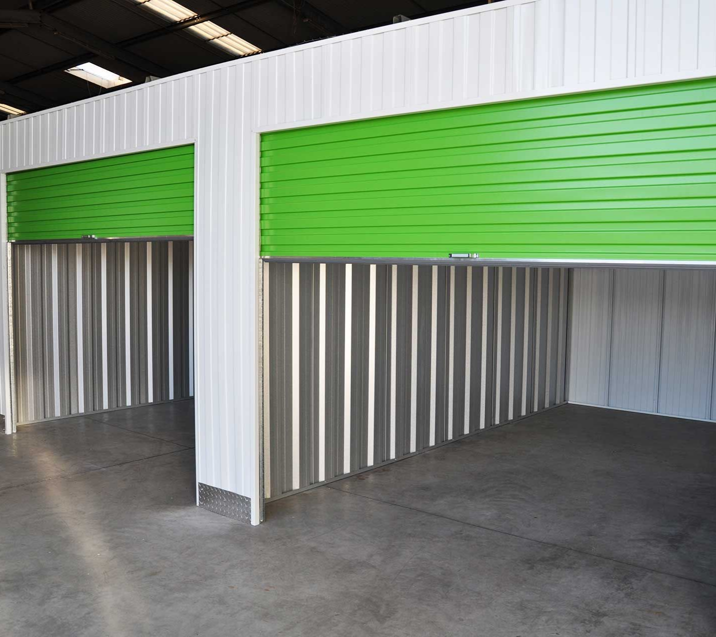 Unités de stockage avec portes sectionnelles vertes et parois en tôle ondulée. Sol en béton. Finitions blanches.