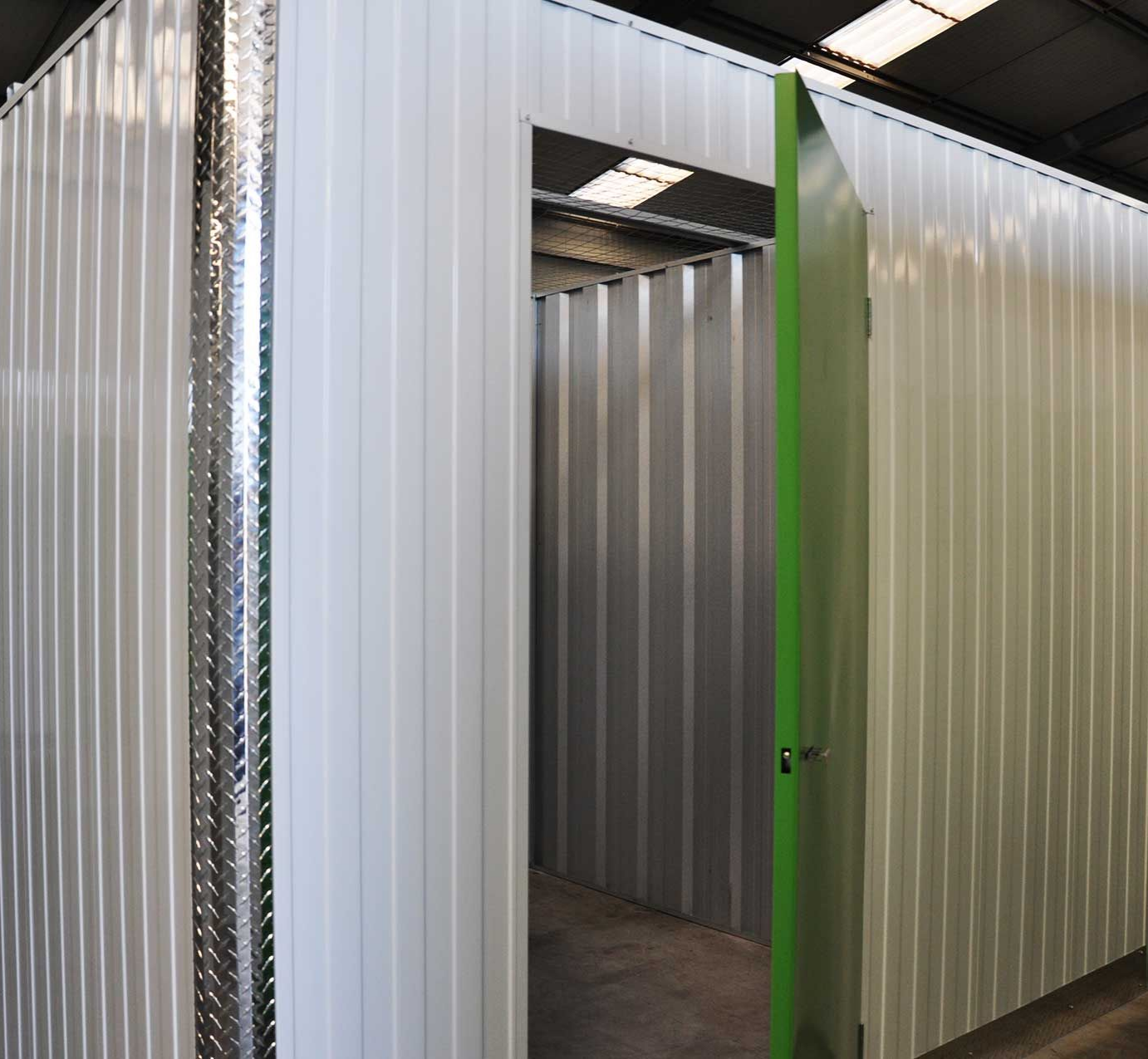 Des conteneurs de stockage en tôle ondulée blanche avec une porte verte ouverte. À l'intérieur, on aperçoit un autre conteneur.