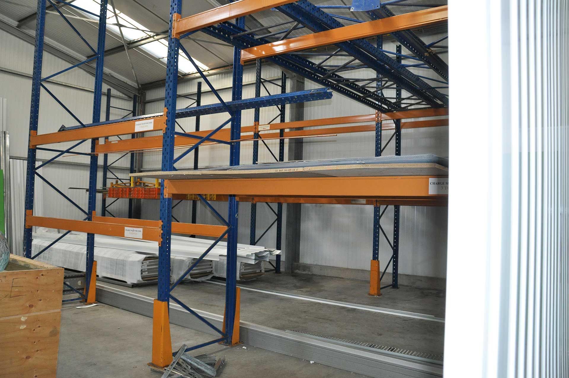 Intérieur d'entrepôt avec des étagères orange et bleues supportant des piles de matériaux.