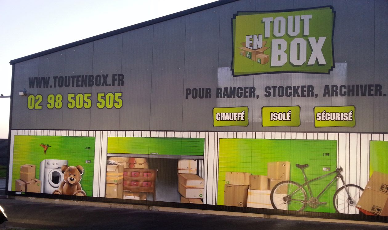 Bâtiment orné du logo Tout Box et d'illustrations d'unités de stockage. Site web et numéro de téléphone inclus.