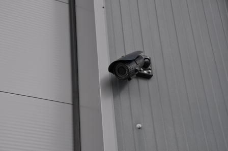 Caméra de sécurité fixée sur un mur en tôle ondulée grise.