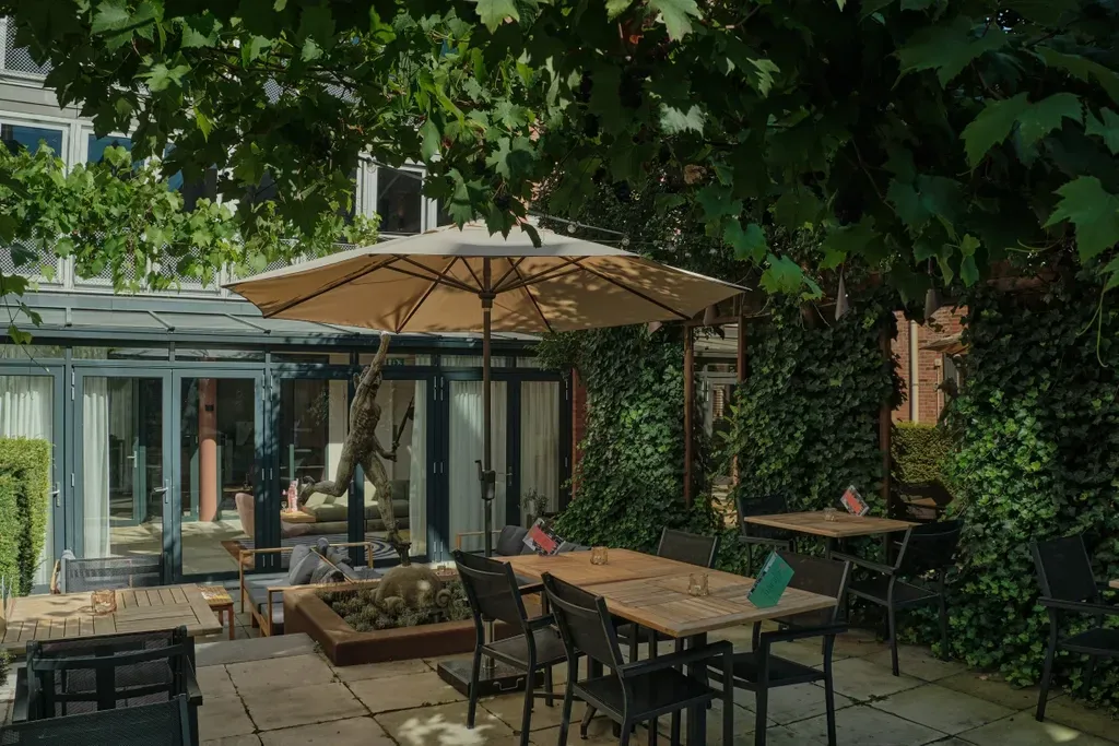 Een terras met tafels, stoelen en parasols voor een gebouw.