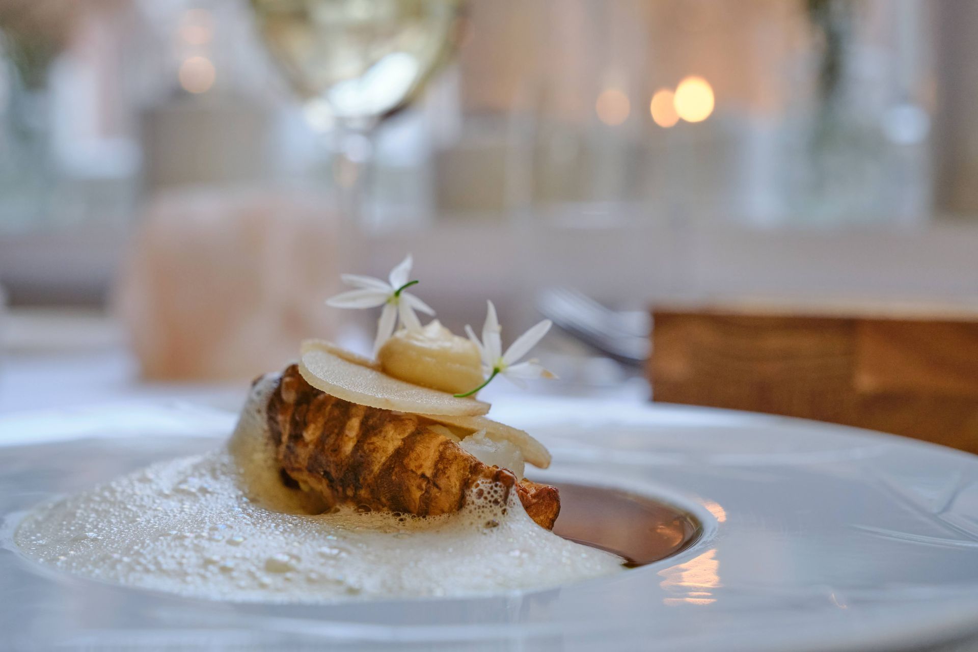 Feestscène in de buitenlucht met mensen verzameld op een binnenplaats. Groen gebladerte omringt een glazen dak; ballonnen en tafels zijn aanwezig.