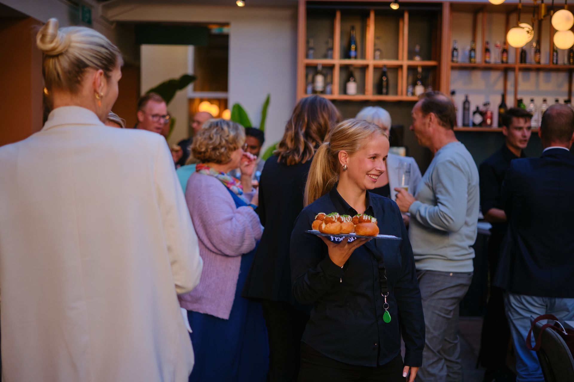 Een vrouw houdt een dienblad met eten vast in een drukke kamer.