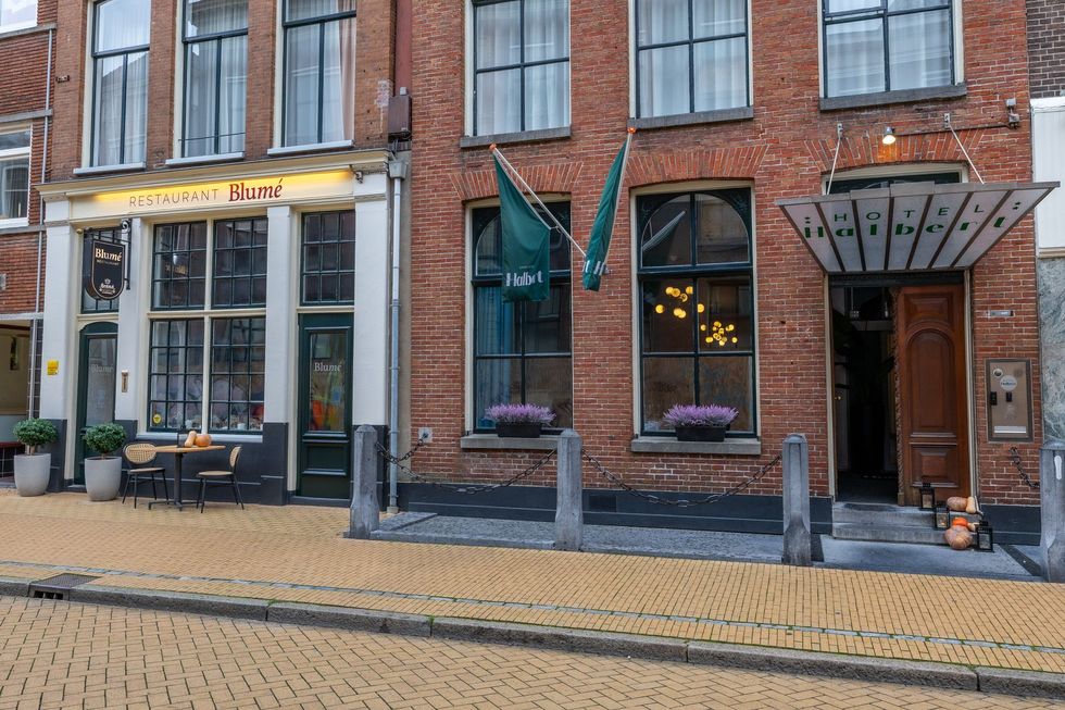 Straatbeeld van twee bakstenen gebouwen met grote ramen. Het gebouw links heeft een café met terras, terwijl het gebouw rechts een hotelingang heeft.