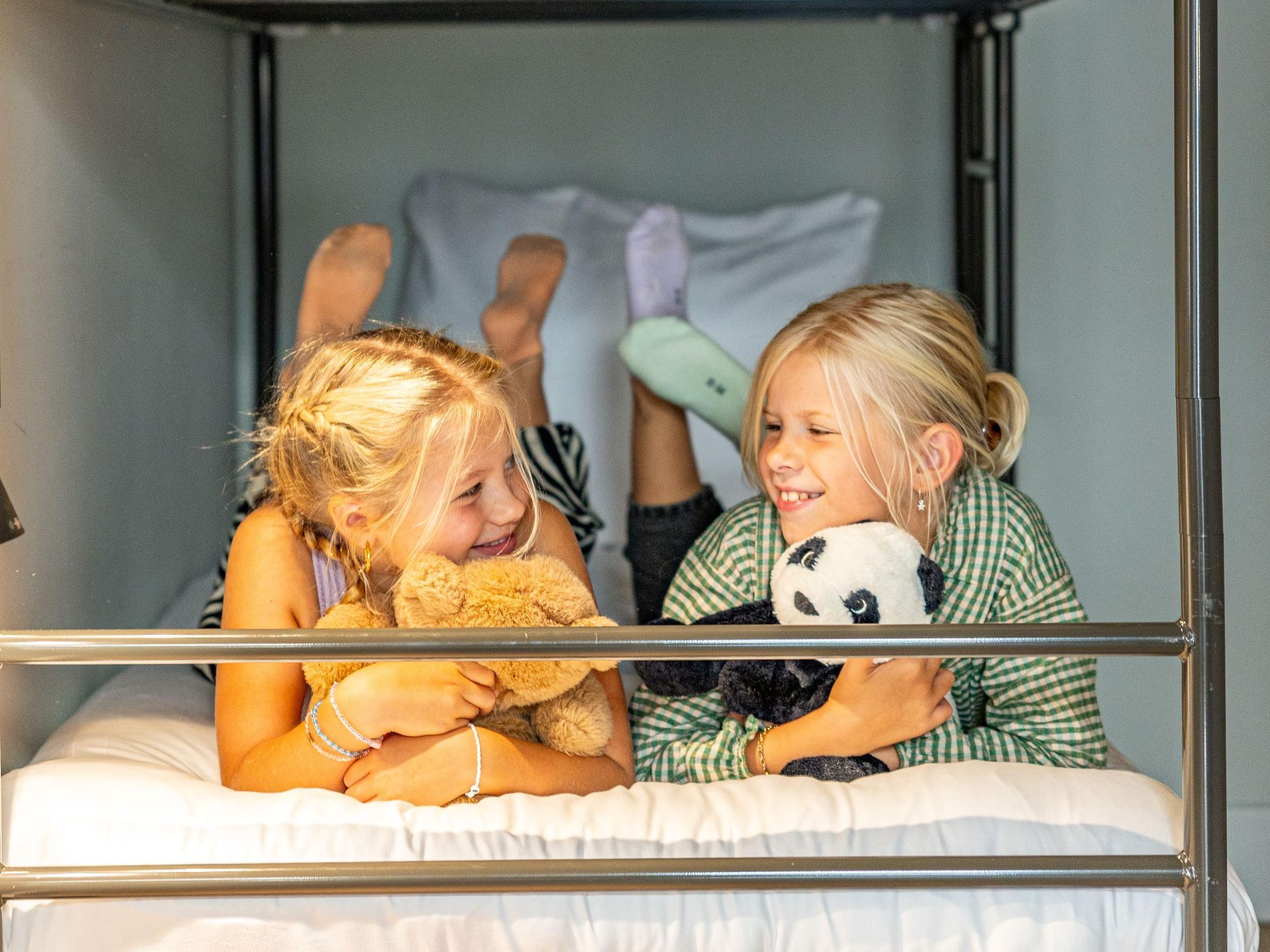 Twee jonge meisjes liggen op een stapelbed en houden knuffels vast.