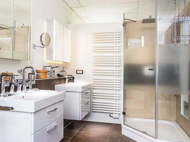 Modernes Musterbad mit Waschtisch, Dusche, Spiegel und Designheizkörper in heller Ausstellung.