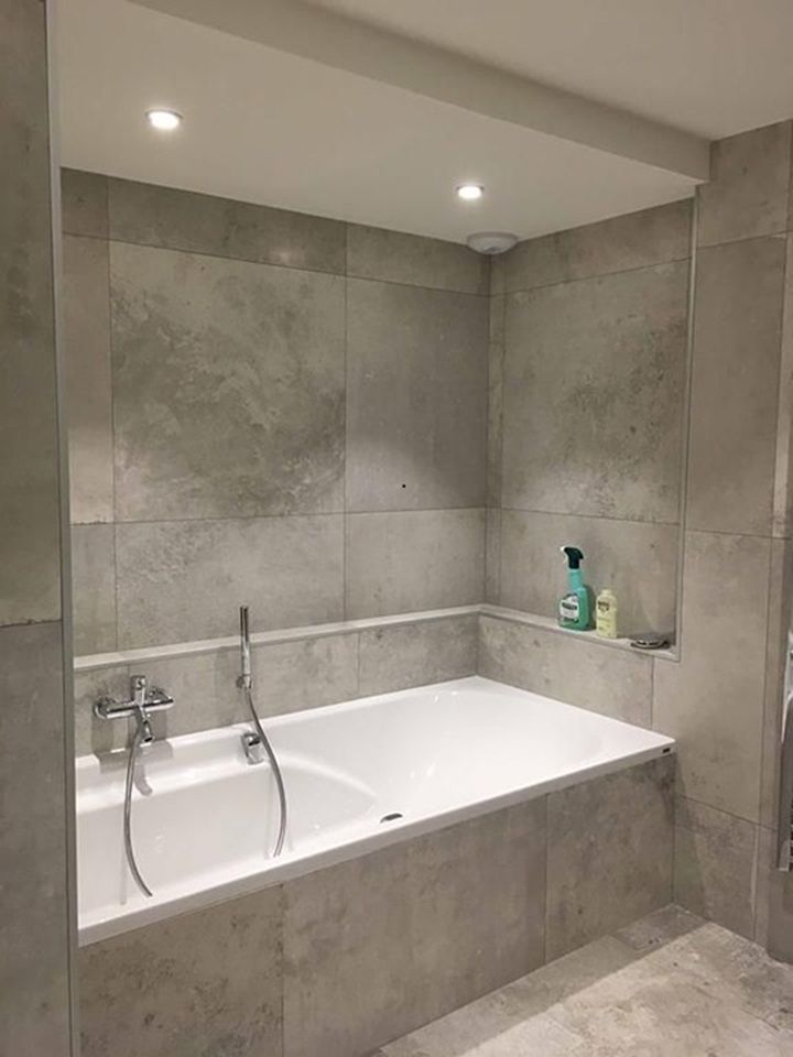 Salle de bains moderne carrelée de gris avec baignoire encastrée.