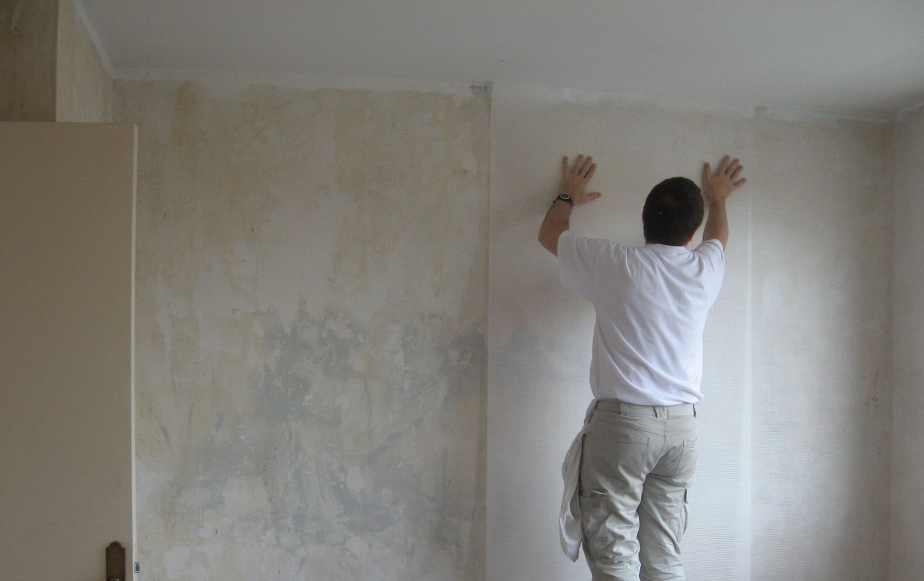 Une personne pose de la toile de verre sur un mur
