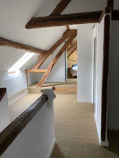 Couloir étroit de type loft avec des poutres en bois apparentes et murs blancs inclinés.