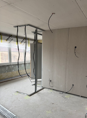 Pièce inachevée avec une structure métallique, des fils électriques apparents et de grandes fenêtres.