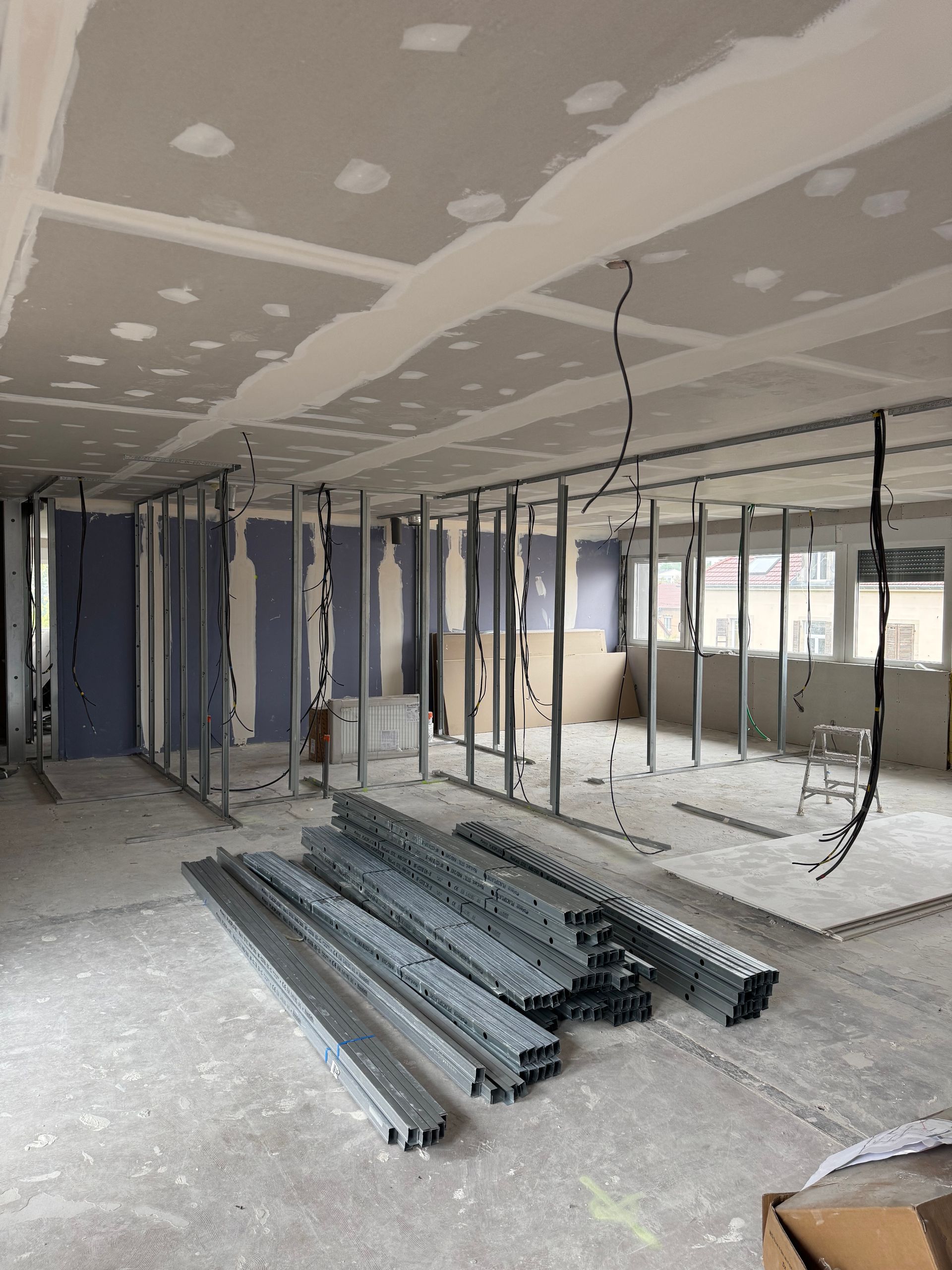 Pièce en construction avec des cloisons sèches, des fils électriques qui pendent et des montants métallique.