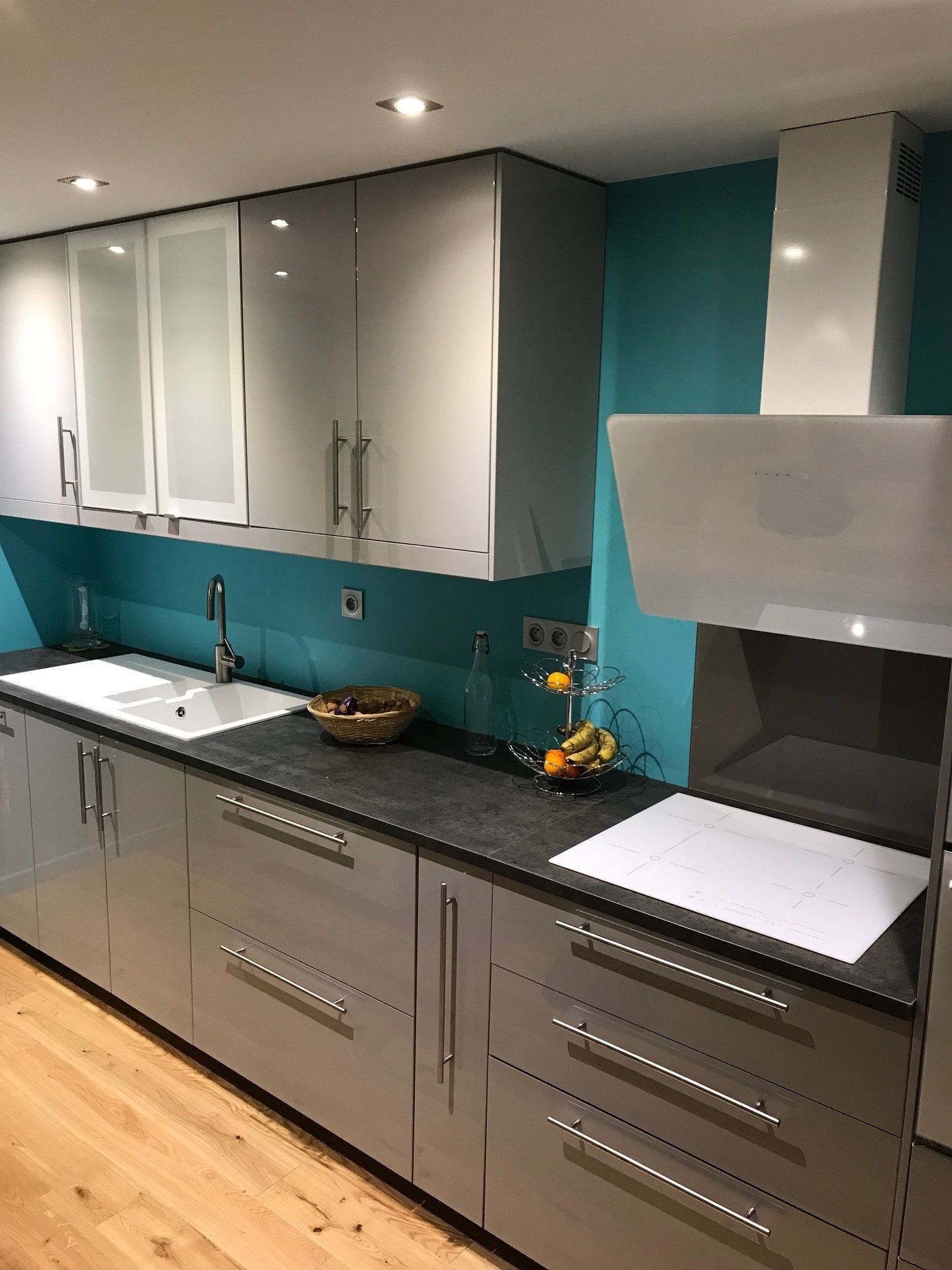 Cuisine moderne avec placards gris, mur turquoise, plan de travail noir, évier et hotte en inox.