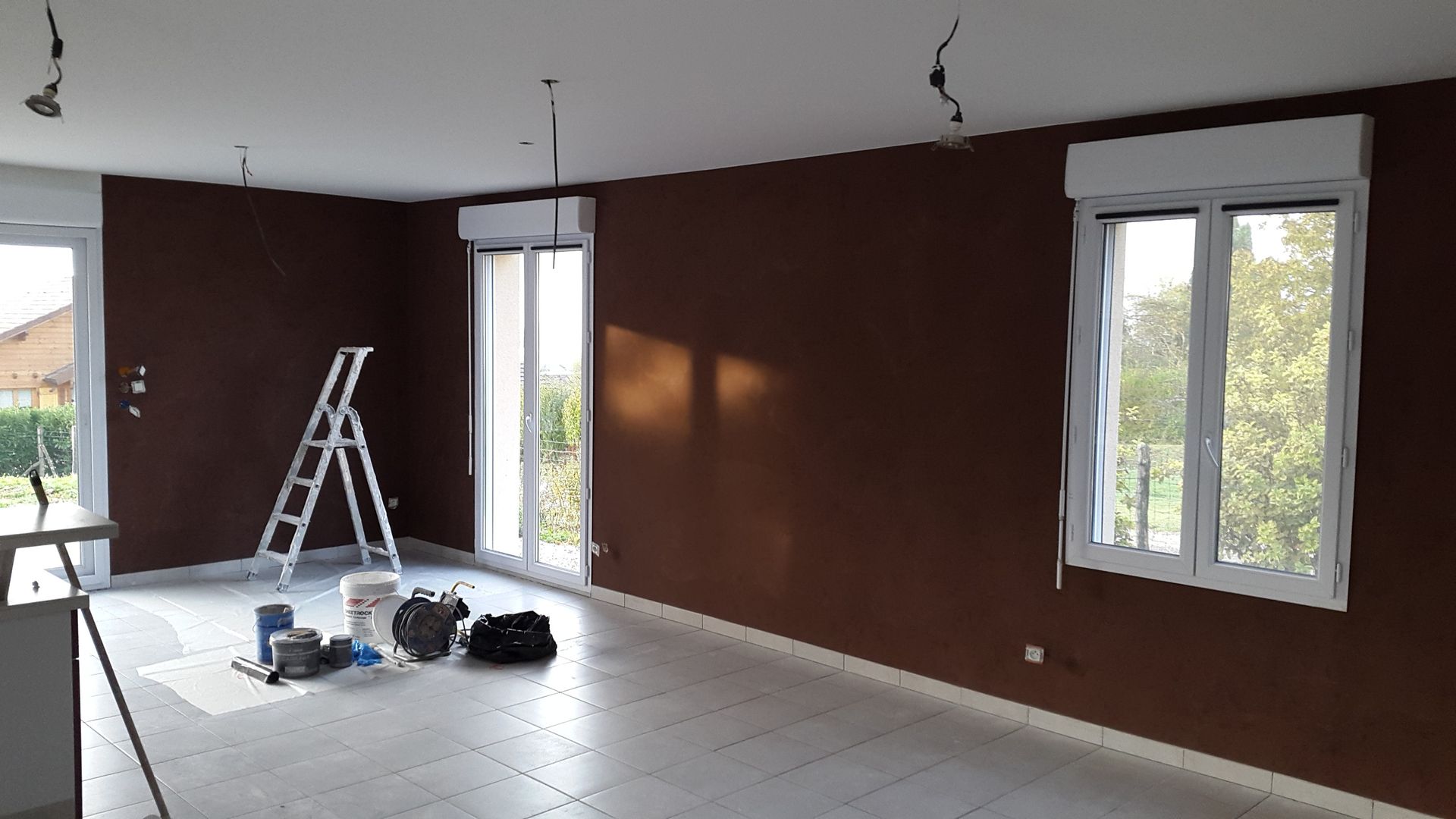 Pièce partiellement aménagée avec des murs marron, un sol carrelé blanc et un escabeau.