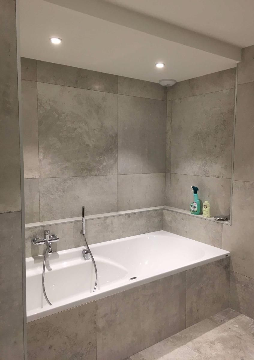 Salle de bains moderne carrelée de gris avec baignoire blanche sous un éclairage encastré