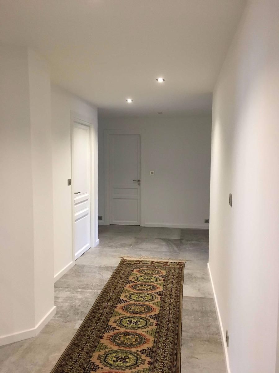 Couloir étroit aux murs blancs, tapis à motifs sous des spots encastrés.