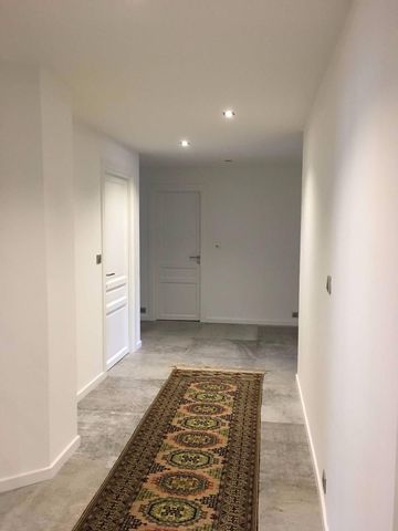 Couloir étroit et blanc, avec sol carrelé gris et tapis à motifs, menant à une porte fermée.