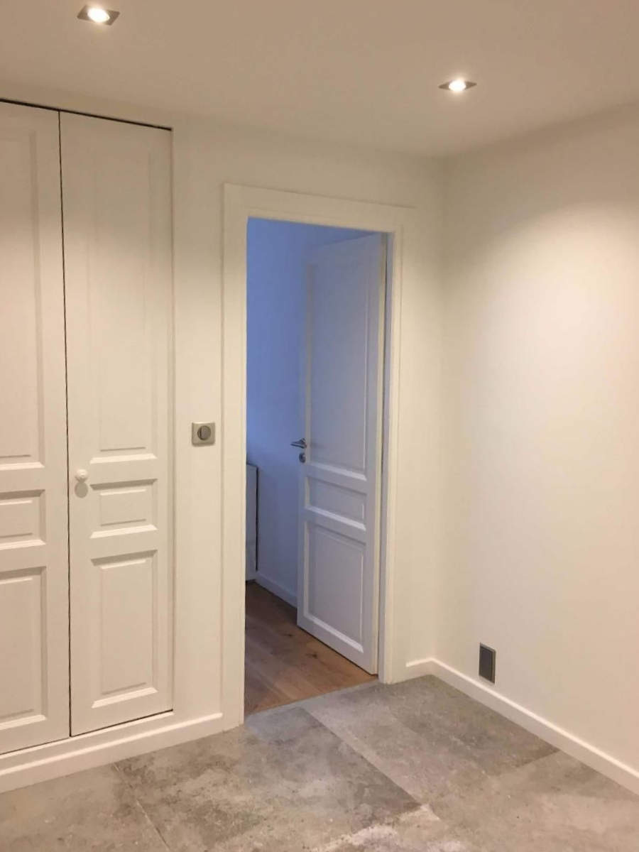 Pièce blanche vide avec porte ouverte, placard intégré peint en blanc sous éclairage encastré