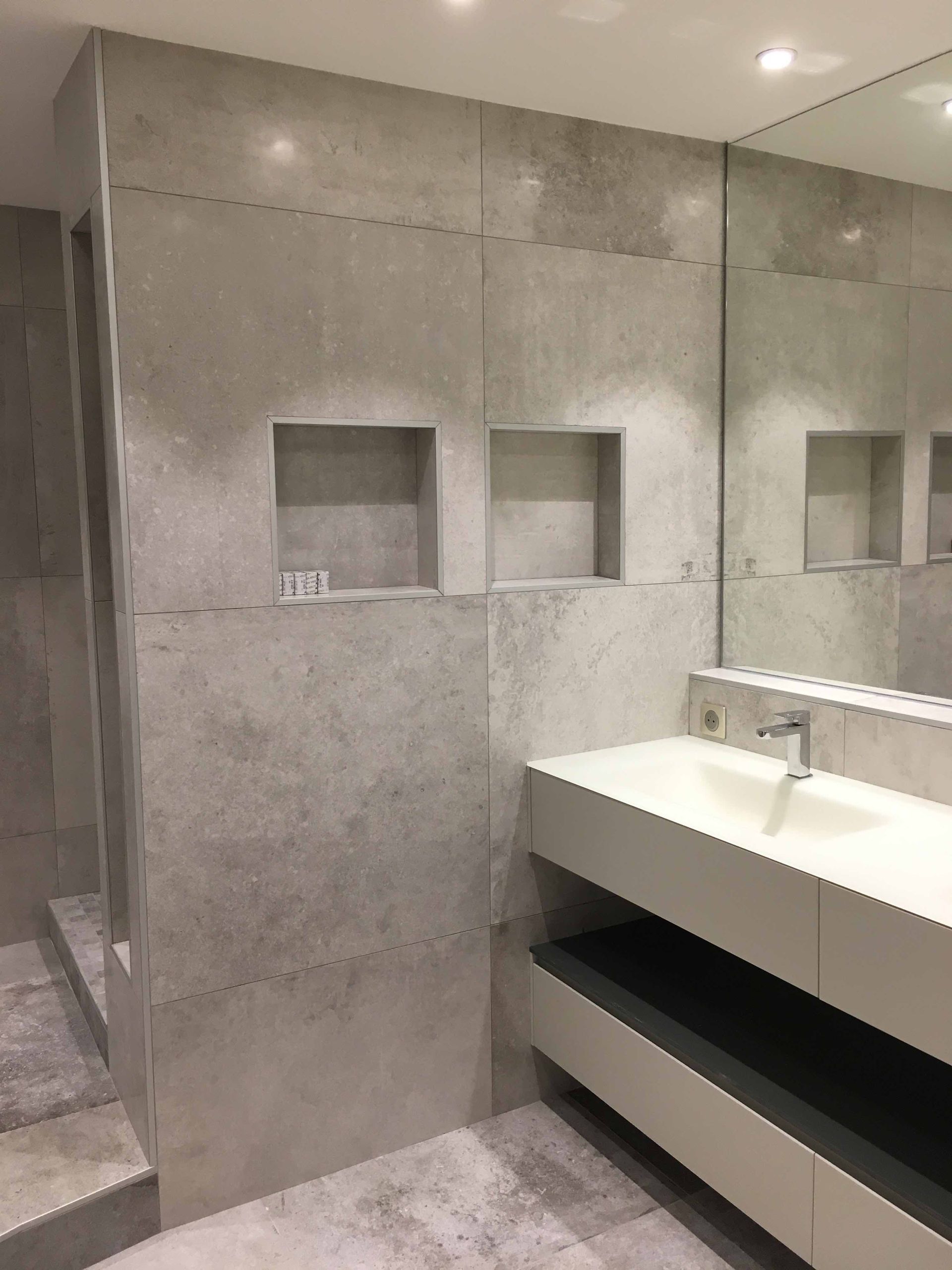 Salle de bains moderne avec murs en béton, meuble-lavabo à double vasque et niches murales encastrées.