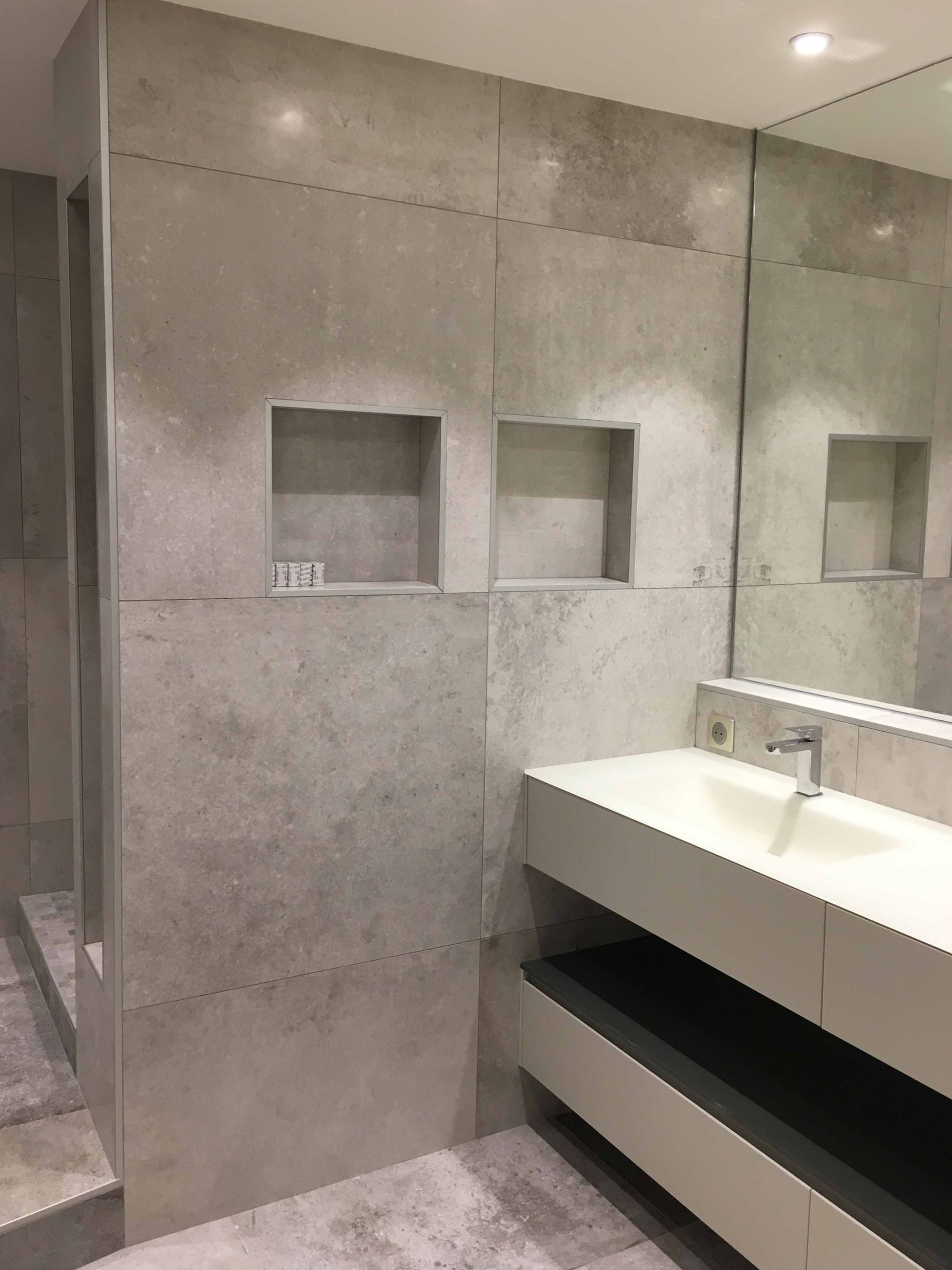 Salle de bains moderne avec mur carrelé, étagères encastrées et meuble-lavabo avec miroir.