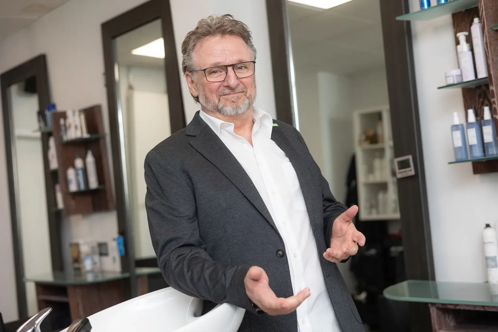 Ein Mann im Anzug steht neben einem Waschbecken in einem Friseursalon.
