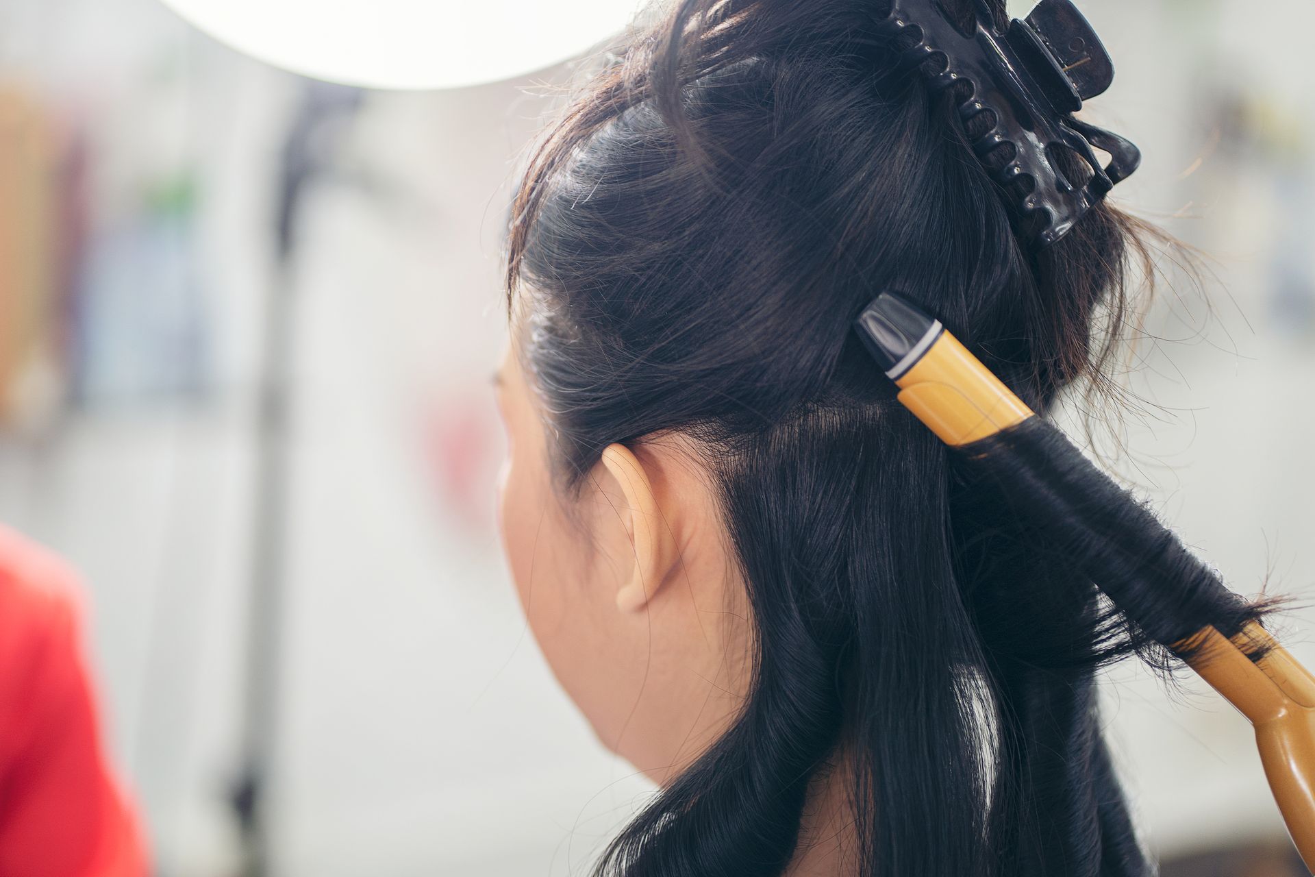 Einer Frau werden die Haare mit einem Lockenstab gelockt.