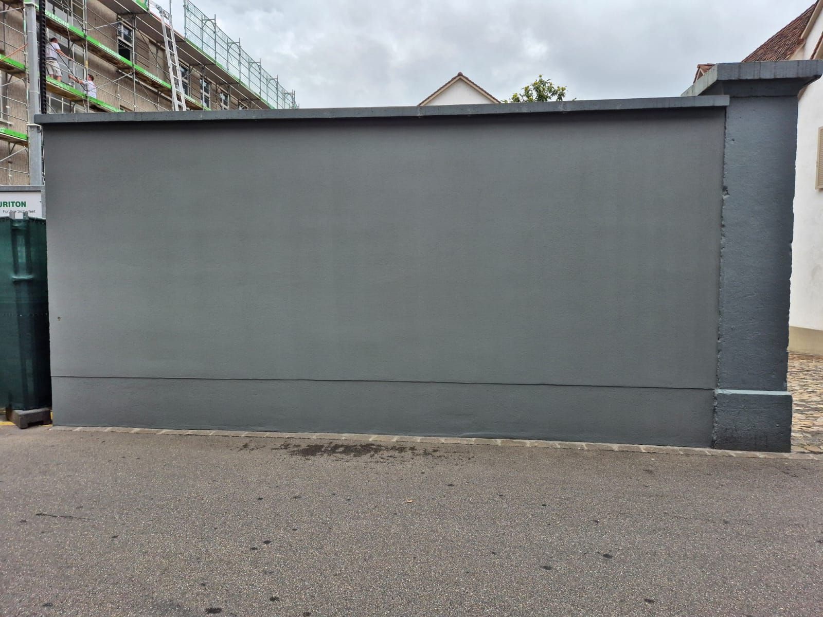 Am Straßenrand steht eine große graue Mauer.