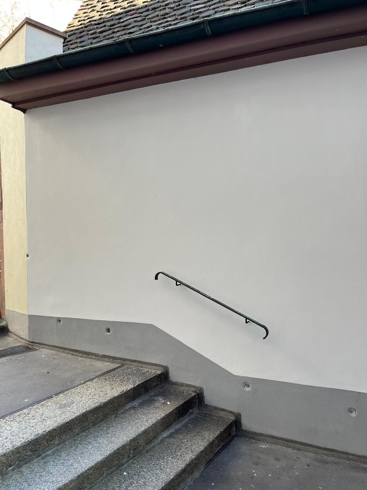 Eine weiße Wand mit hinaufführenden Stufen und einem Handlauf.