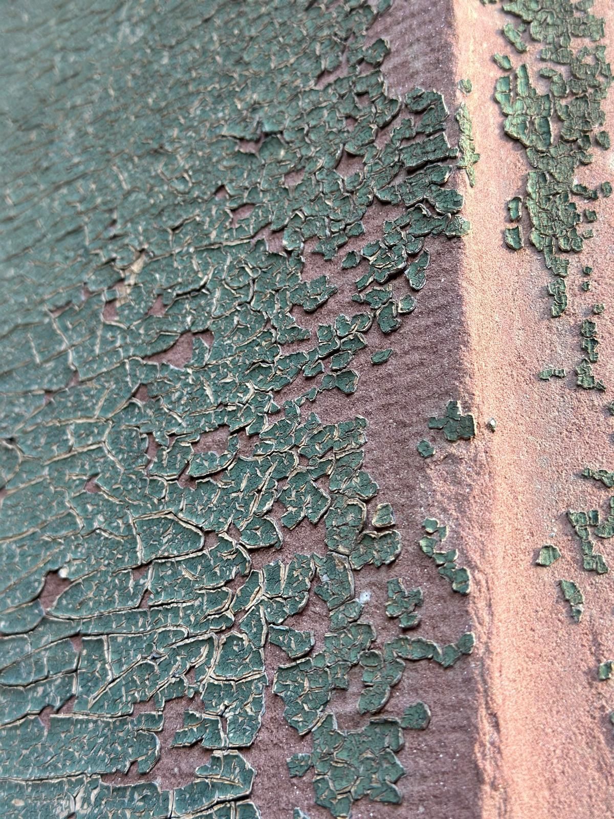 Eine Nahaufnahme von rissiger grüner Farbe auf einer braunen Oberfläche.