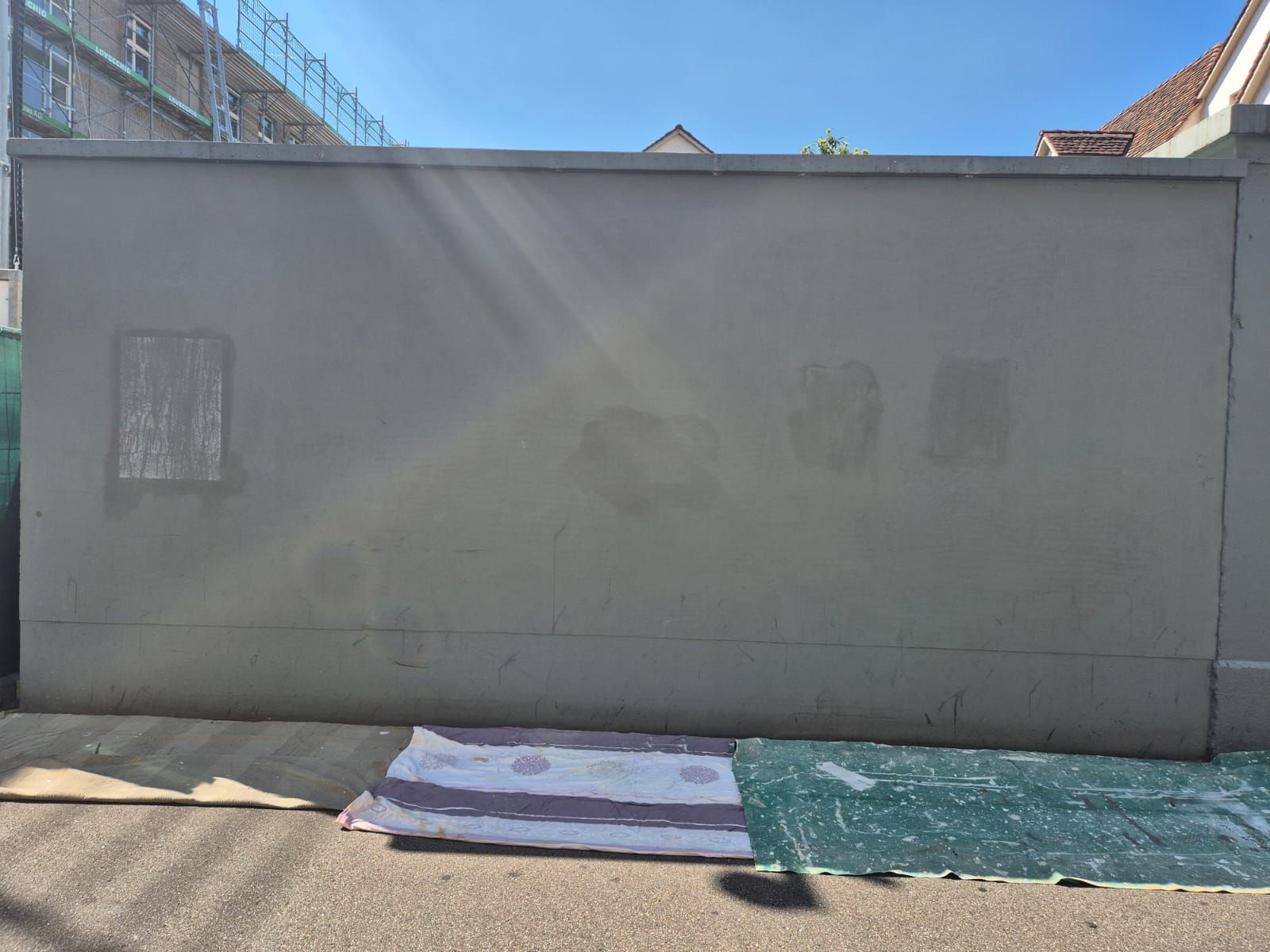 An einem sonnigen Tag wird eine große graue Wand gestrichen.