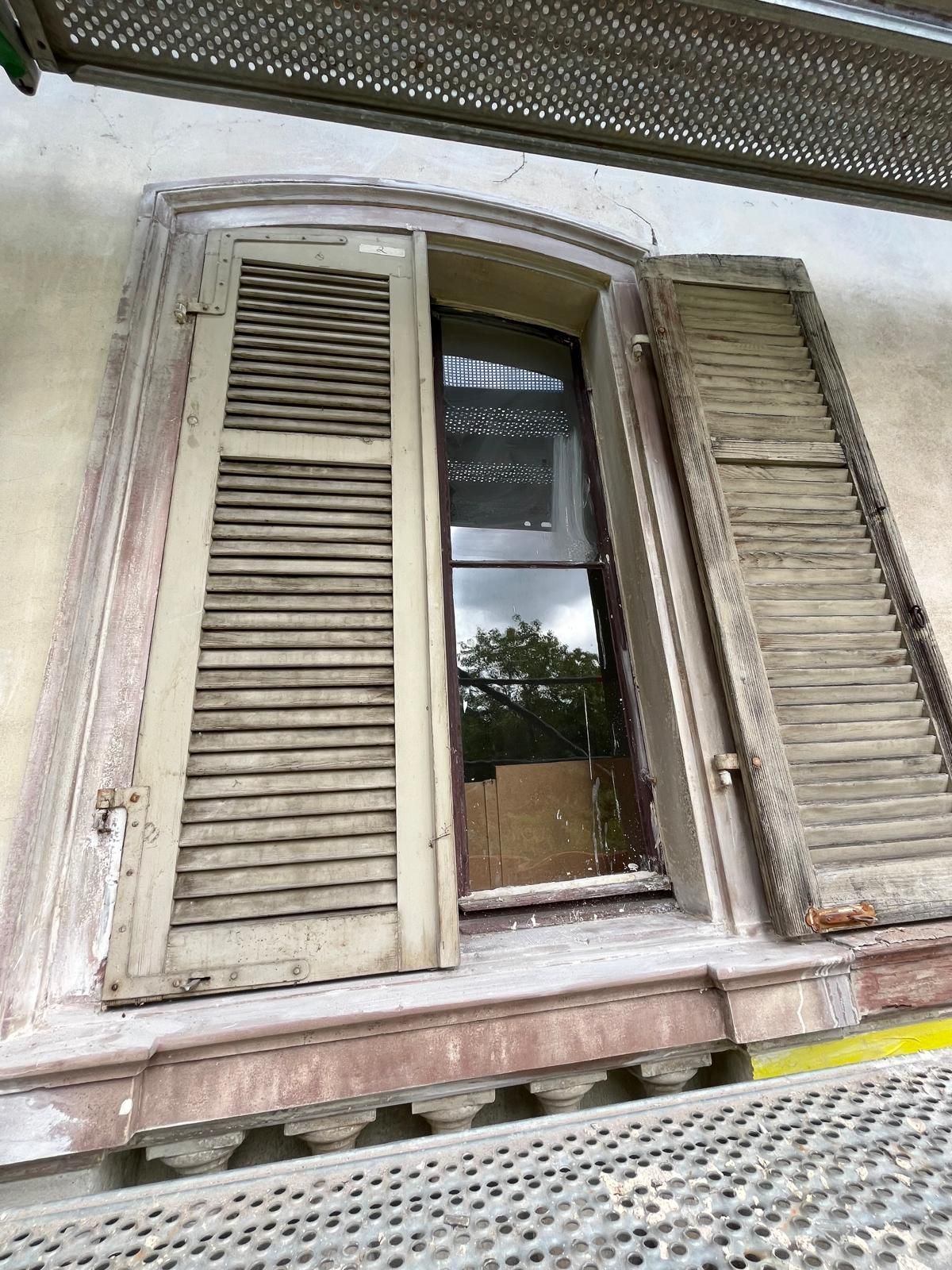 Auf einem Gerüst steht ein Fenster mit Fensterläden.