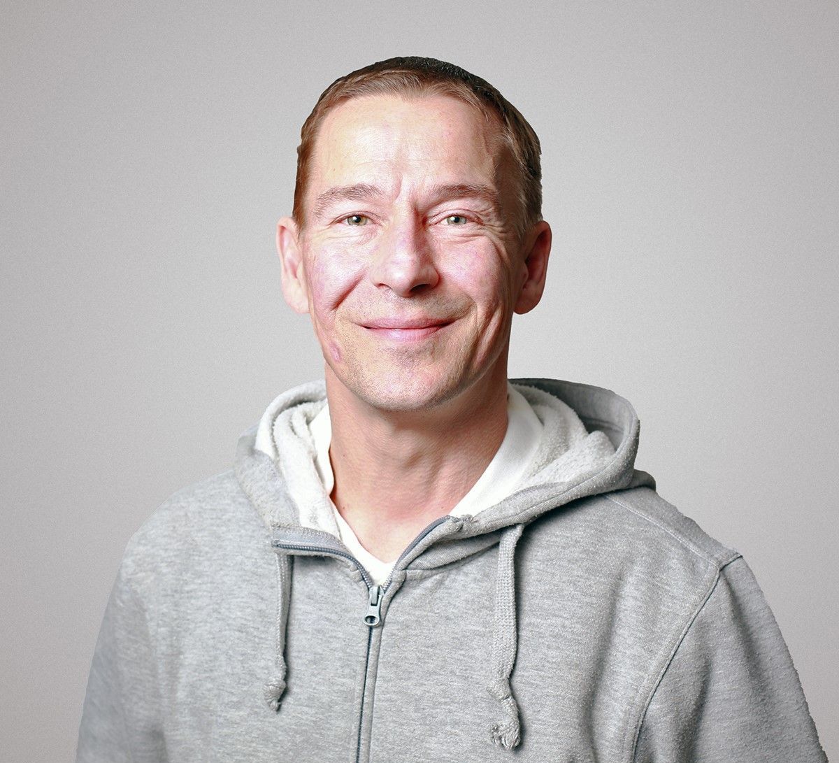 Ein Mann mit einem grauen Kapuzenpullover lächelt in die Kamera.