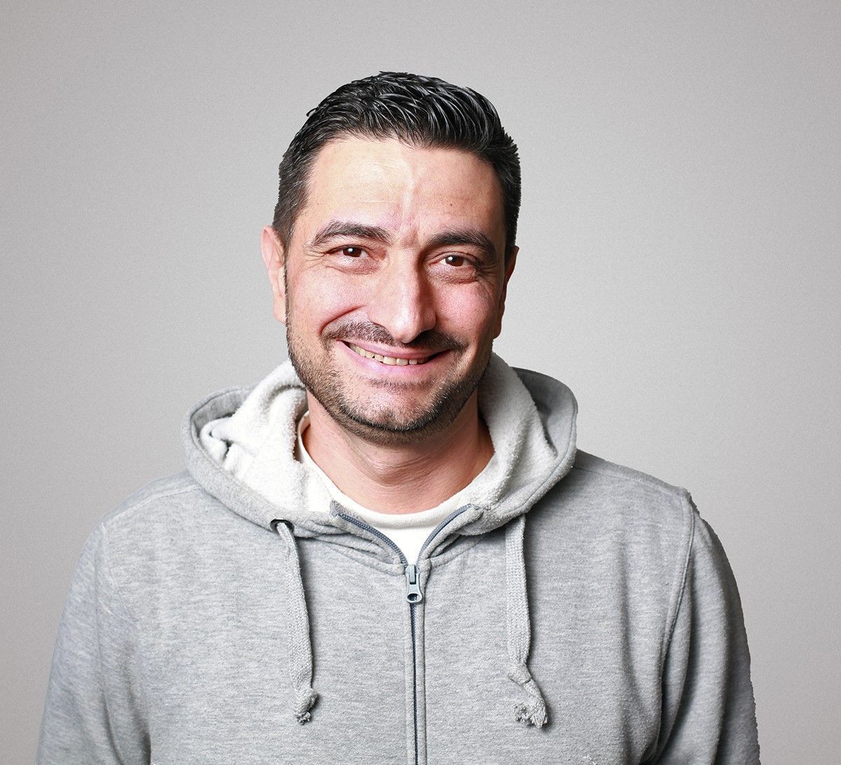 Ein Mann mit einem grauen Kapuzenpullover lächelt in die Kamera.