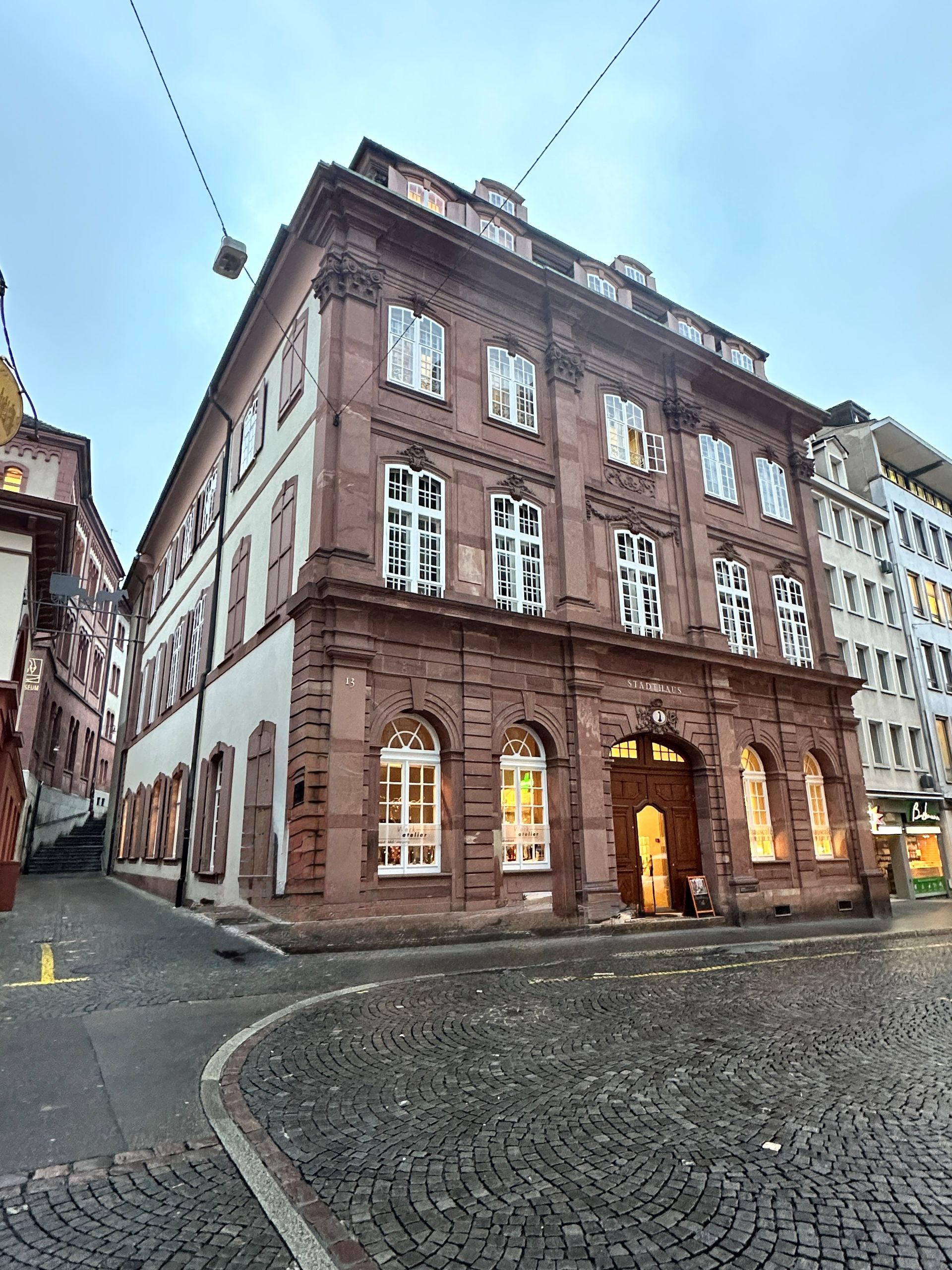 An der Ecke einer Kopfsteinpflasterstraße steht ein großes Gebäude mit vielen Fenstern.