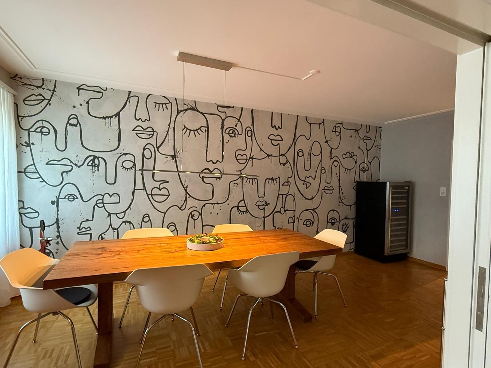 Ein Esszimmer mit einem Tisch und Stühlen und einer Wand mit Gesichtszeichnungen darauf.