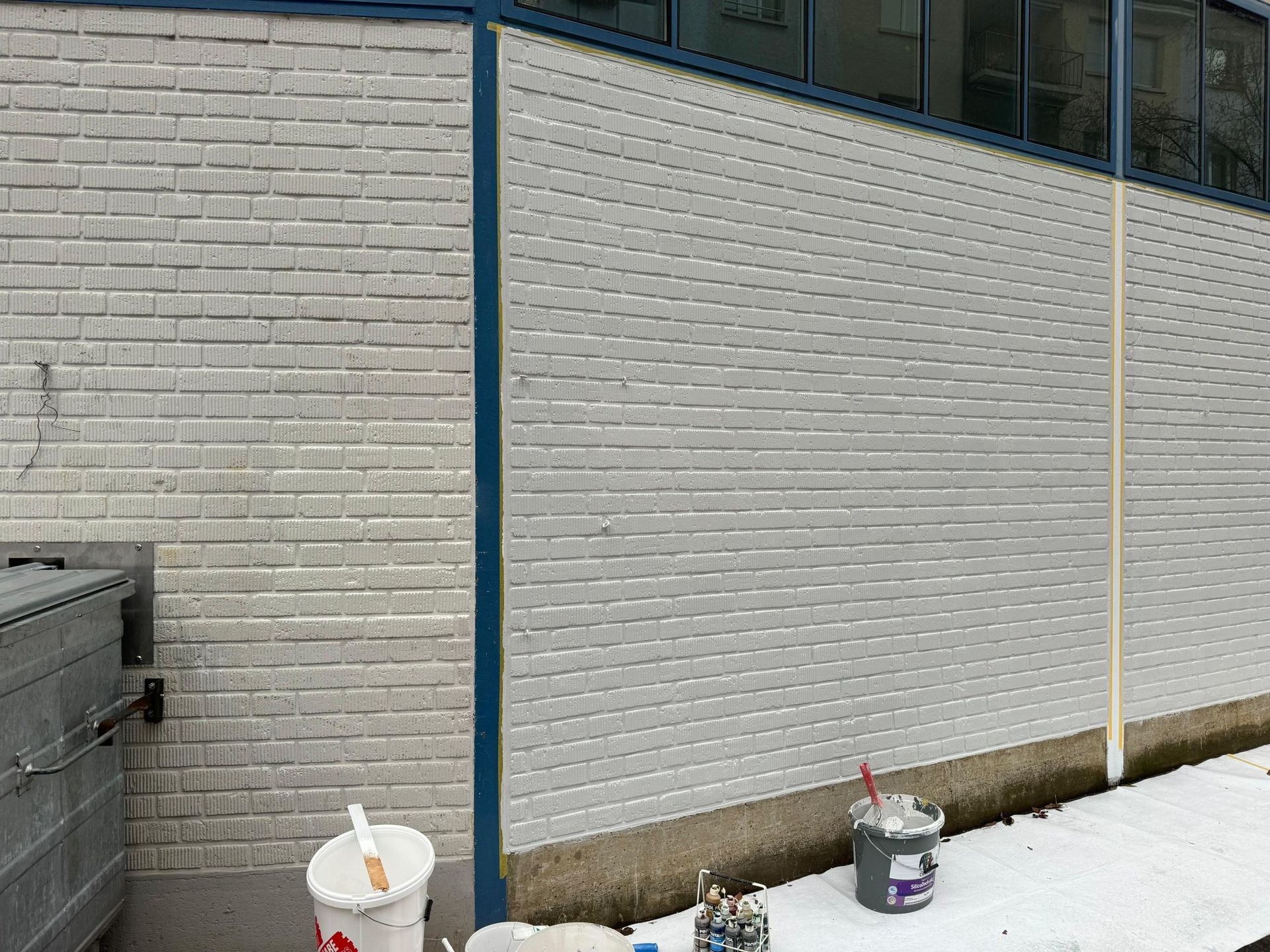 Eine weiße Ziegelwand mit Farbeimern und Pinseln davor.