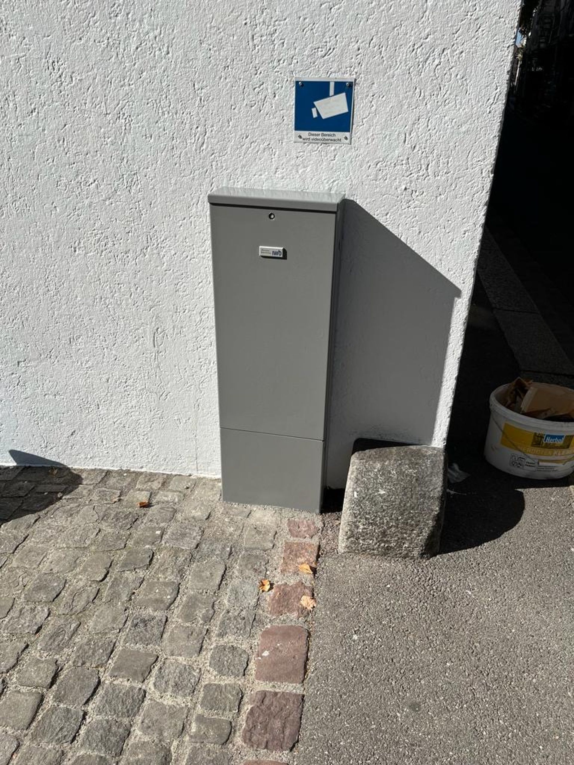 An der Seite eines Gebäudes neben einem gepflasterten Gehweg steht ein Briefkasten.