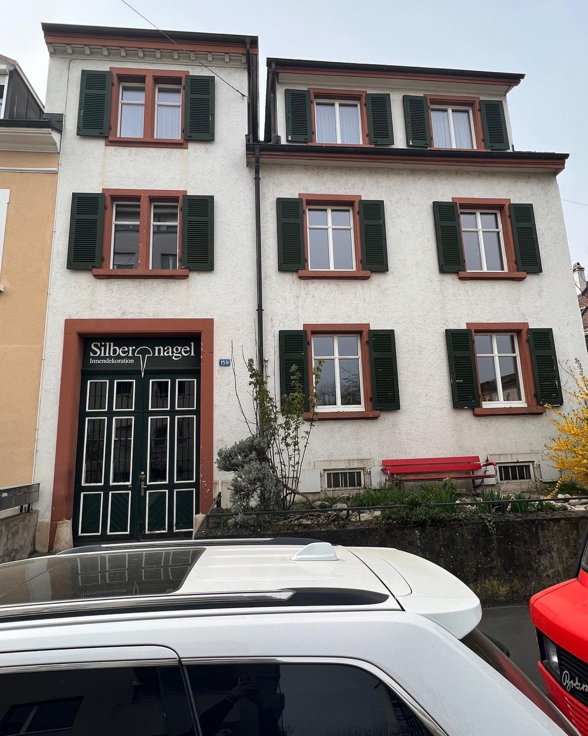 Ein Auto parkt vor einem weißen Gebäude mit grünen Fensterläden