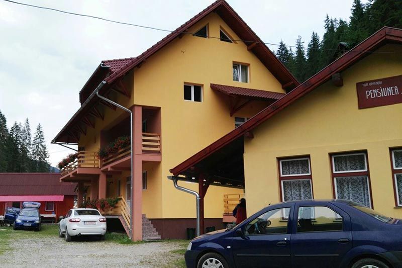 Un coche azul está aparcado delante de un edificio amarillo con techo rojo.