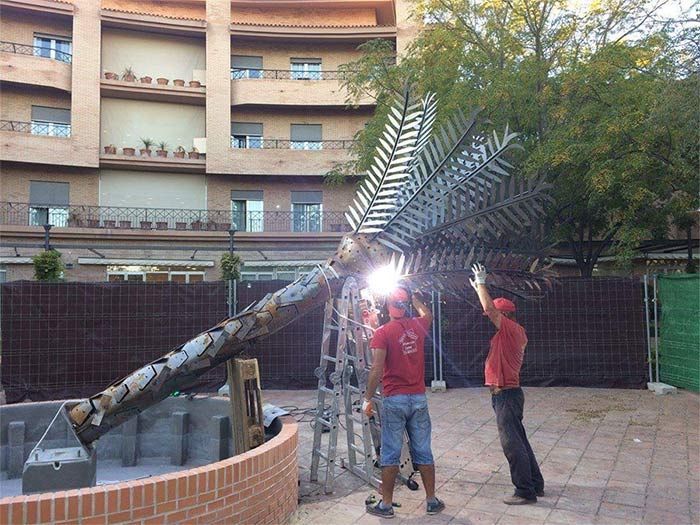 Dos hombres están soldando una palmera frente a un edificio.