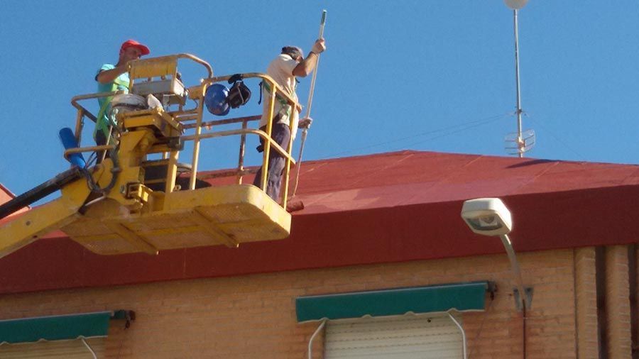 Un hombre está pintando el techo de un edificio con una grúa.