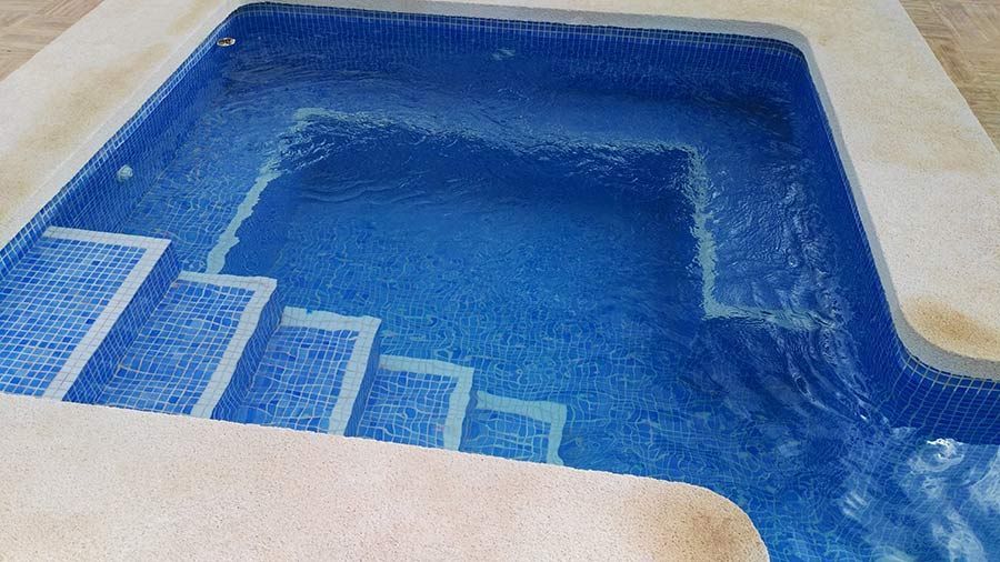 Una piscina con azulejos azules y escaleras blancas.
