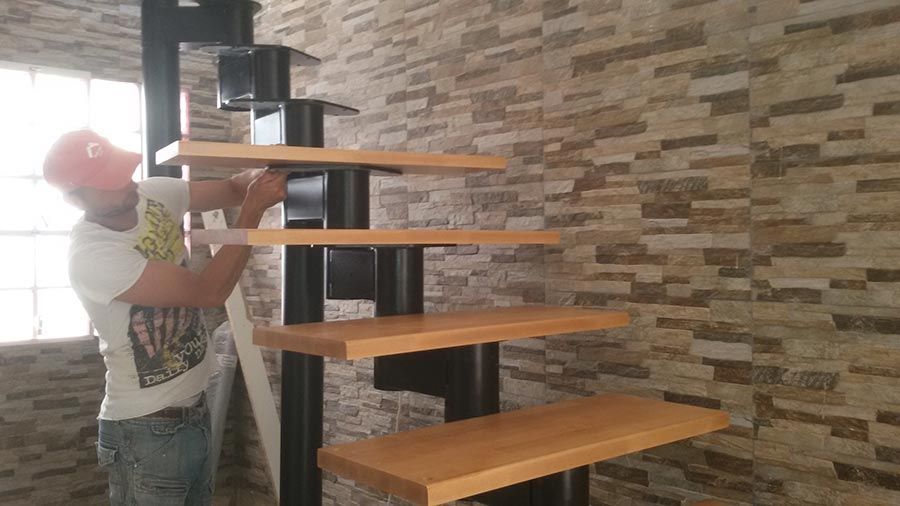 Un hombre está de pie junto a una escalera de madera en una habitación.