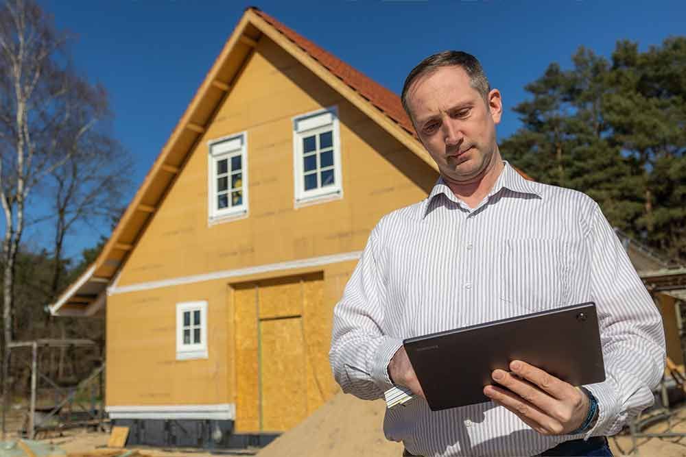 Ein Mann hält ein Tablet vor einem im Bau befindlichen Haus.