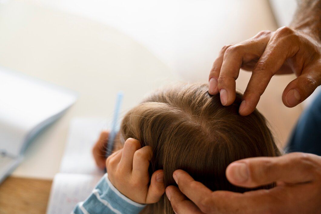 Manos enguantadas peinando el cabello castaño de un niño mientras este sostiene su cabeza en una sala de estar.